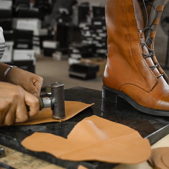 Skilled craftsman using tools to create leather boots in an industrial setting.